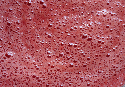 A red foam with air bubbles is located on on the surface of the squeezed tomato juice. Close-up.