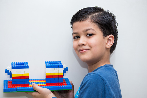 a six year old Indian boy showing his creative and architectural skills by making a building structure with building blocks toys