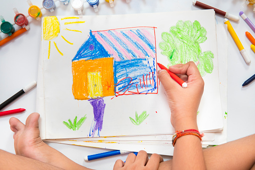 High angle close-up image of cropped hands making drawing of house, tree, and filling colors.