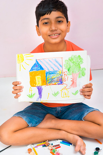 Happy young boy showing his colorful house drawing art and looking at camera with smile.
