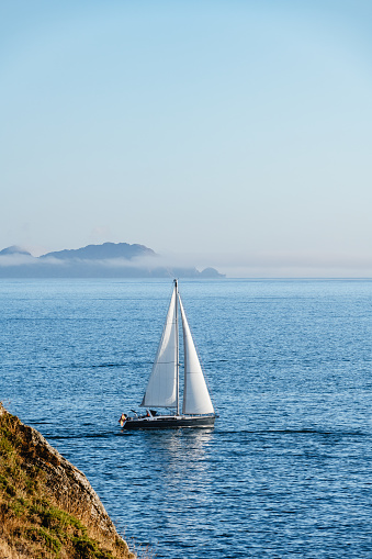 A lonely boat sails away from the Ria de Pontevedra in Galicia at dusk, with the Cies Islands in the background.