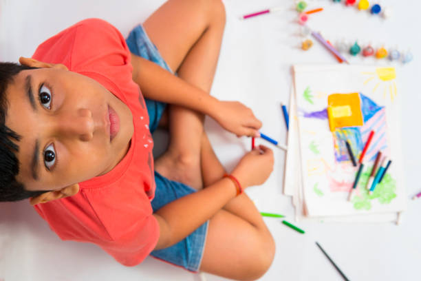 Top view image of young boy making drawing and looking at camera.