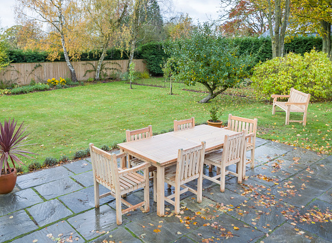 Large UK back garden in autumn with wooden furniture on a garden patio terrace