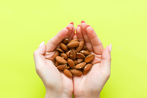 A hand holding almonds on a light green background