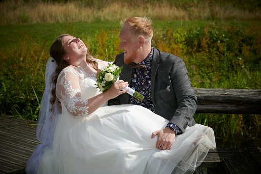 Bride and Groom sitting on bench outdoors in park having fun and laughing