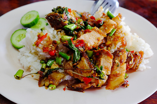Rice topped with Stir Fried Spicy Crispy Pork and Thai basil on white plate.Tradition Thai food.