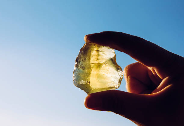 Person hand holding one yellow green lemon quartz crystal stone against sun and blue sky. Shiny, copy space. Person hand holding one yellow green lemon quartz crystal stone against sun and blue sky. Shiny, copy space. geode photos stock pictures, royalty-free photos & images