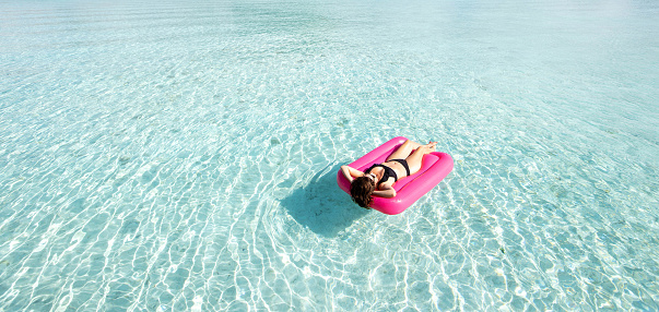 a woman floats over tropical island Bora Bora turquoise ocean water while on a pink inflatable mattress providing color contrast