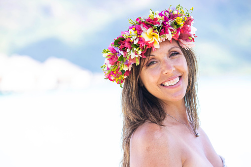 A beautiful woman with a bright smile wears a flora crown filled with colorful tropical flowers