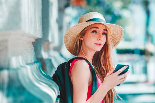 istock Pretty young woman wearing straw hat and backpack while standing on the street 1278285618
