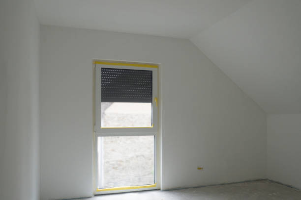 White empty ready-to-paint room with attic ceiling,French window,gray concrete floor.Roller shutter is third down.Design of attic bedroom with sloping roof,panoramic window,Germany.Copy space,mock up. habitación blanca vacía lista para pintar con techo en el ático, ventana francesa, suelo de hormigón gris. el obturador del rodillo está en tercer lugar hacia abajo. diseño del dormitorio del ático con techo inclinado, ventana panorámica, alemania.