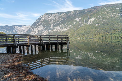 Morning view of Lake Bohinj with fog, mountain reflecting in tranquil lake water, and wooden pier, Julian Alps, Slovenia