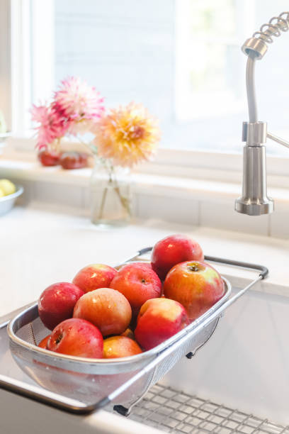 Freshly washed apples in a strainer rack in sink. Vertical. Modern Farmhouse style, dahlias in background. High Key. Plenty of copy space. stock photo