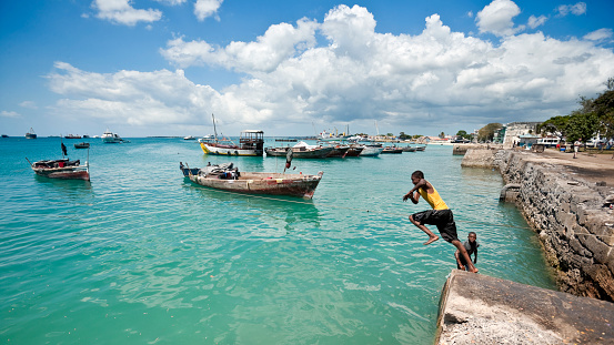 Stone Town, Zanzibar, Tanzania | October 21, 2007: Teenagers jumping in the turquoise sea at the harbour