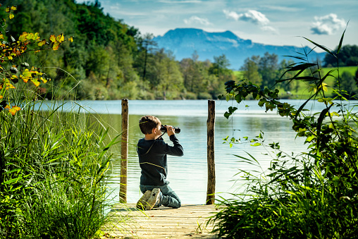 Austria, upper austria, Hoellerersee. Little Boy with a binoculars at a wooden footbridge at the Hoellerer See in Upper Austria in the area of ​​the municipalities of St. Pantaleon and Haigermoos. The lake is 780 m long, 330 m wide and has the shape of a kidney; the maximum depth is 21 meter.