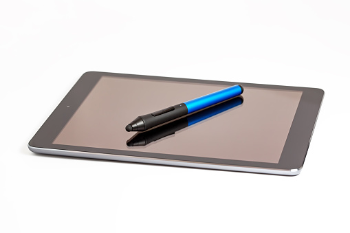 A modern black tablet computer with a blank screen and a wireless stylus on top. The tablet lies on a white background and is turned at some angle to the viewer. Technology concept