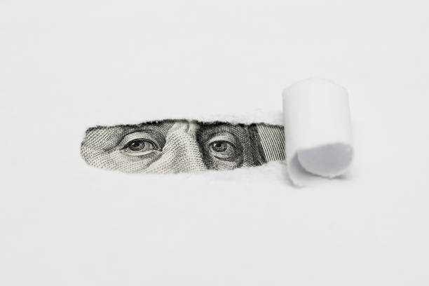 istock Benjamin Franklin macro peeking through torn white paper. Portrait of Benjamin Franklin, is depicted on the banknote one hundred dollars USA peeking through broken old sheet of paper 1278299665