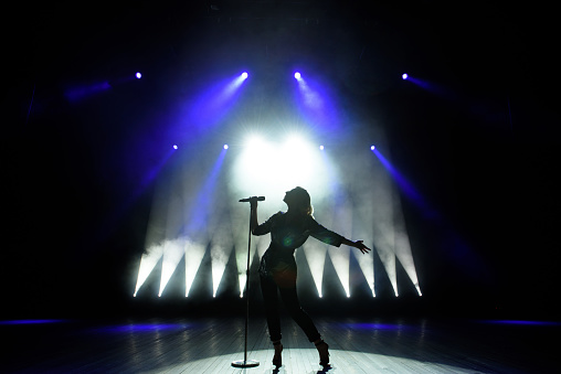 Silhouette of singer on stage. Dark background, smoke, spotlights