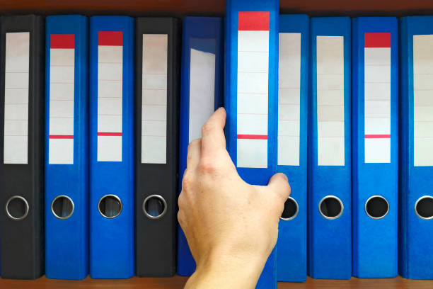 office worker che prende una cartella nell'archivio: concetto di database, amministrazione e gestione dei file. mano ravvicinata che seleziona una grande cartella dagli scaffali con i file di office - archivista foto e immagini stock