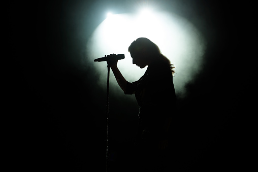 Black silhouette of female singer with white spotlights in the background.