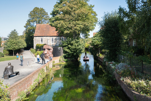 Canterbury, UK - Sep 27th 2020 Tourists enjoy a ride in a punt on the river Stour as it runs past the statue of the Bulkhead by Rick Kirby