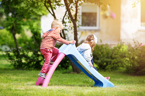 Boy and girl playing on the backyard on sliding.