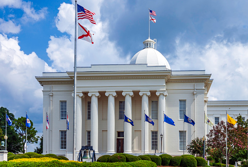 Montgomery Alabama State Capitol building with columns, steps,  Dome, flag and Clock showing