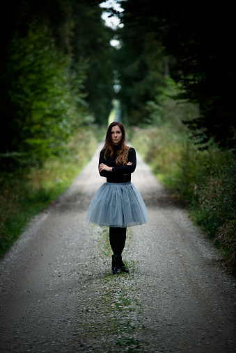 Austria, upper austria. Young woman in a grey dress stand on a long path in a forest.