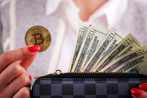 Virtual cryptocurrency money Bitcoin golden coins in the left hand of a woman with red nail polish and a purse. The future of money. US dollars.
