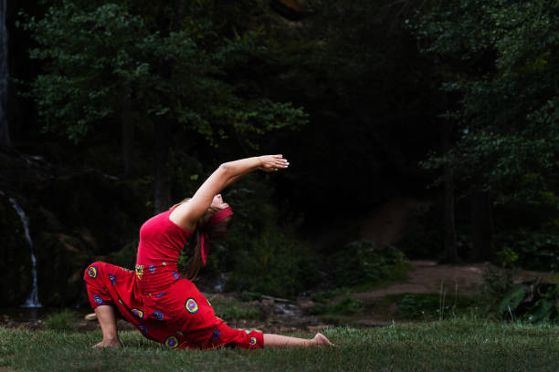 ritratto frontale di donna caucasica adulta di 30 anni seduta su roccia nella natura indossare abito rosso che si estende nella posa yoga nel giorno - spiritualità pace interiore e relax concetto copia spazio - waterfall zen like women meditating foto e immagini stock