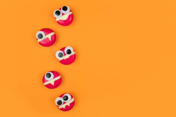 Cheese in form of little monsters with eyes on orange backdrop. Halloween decor for party. Space for text. Food art