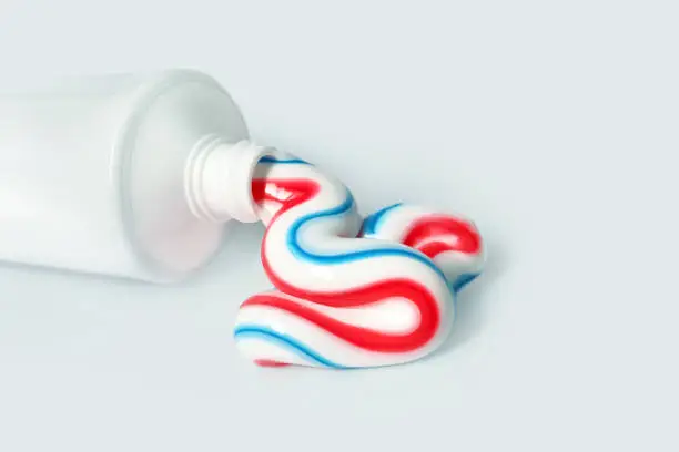 Dental hygiene product. Tricolor toothpaste, copy space. White tube with toothpaste isolated on light background