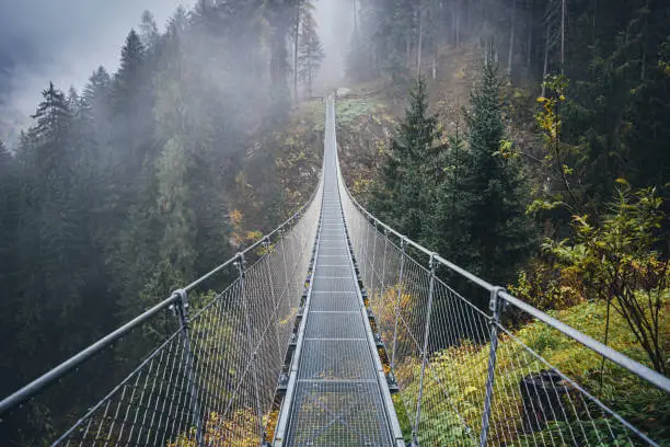 Suspended metal bridge over beautiful rabby valley in fog somewhere in northern Italy in early autumn.