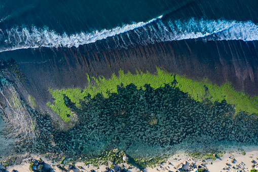 Taken directly from above by drone, abstract horizontal view of a sea coastline lagoon composed by rocks and algae with ocean waves coming in. The scenery was taken in Bali Indonesia.