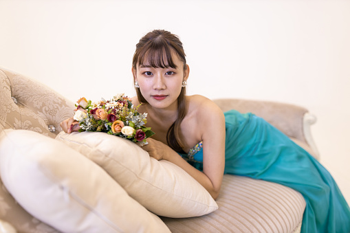 Portrait of young woman in turquoise blue dress holding bouquet on couch
