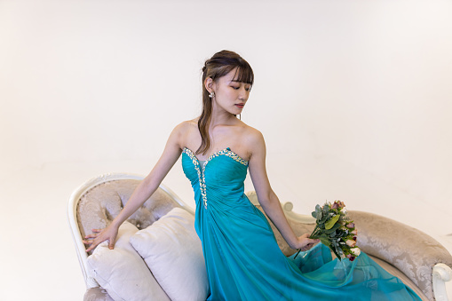 Portrait of young woman in turquoise blue dress sitting on couch