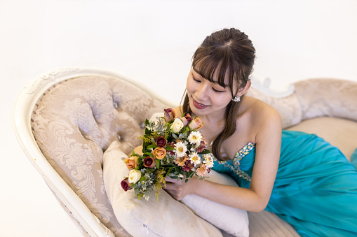Young woman in turquoise blue dress sitting on couch and looking at bouquet