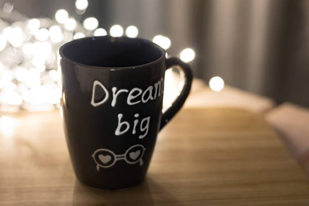 istock Grey mug with text Dream big on a wooden cutting board and lights bokeh on background. Copyspace 1278342490