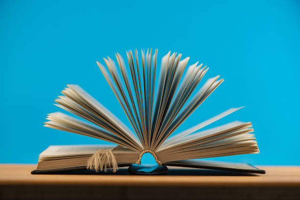 istock Pages of an open book lying on an oak table against a blue background. 1278366421
