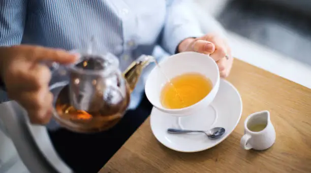 Unrecognizable woman pouring hot tea from teapot, enjoying her morning before work.