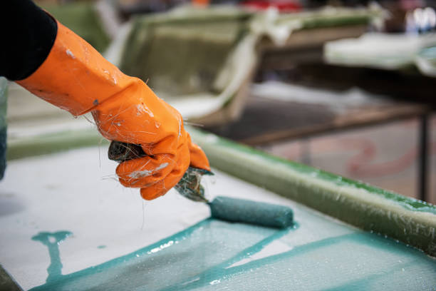 istock Worker's hand in orange glove rolling solution on fiberglass sheet at a factory 1278370430