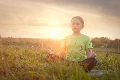Young girl in yoga pose on the meadow in sunset light
