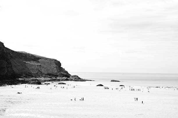 Black and white minimalist seascape. Waves roll into shore and break against tall cliffs. Rugged north Cornish coast during a storm in summer
