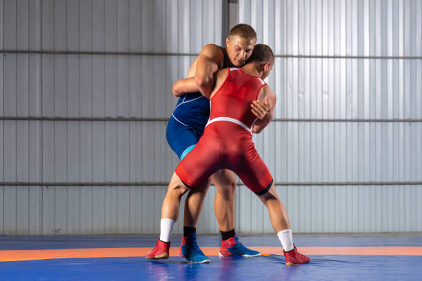 Two young sportsmens Two young sportsmens wrestlers in red and blue uniform wrestling against wrestling carpet, view side wrestling sport stock pictures, royalty-free photos & images