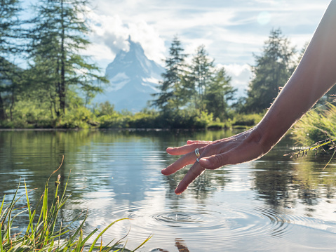 Female hand touching fresh water from mountain lake