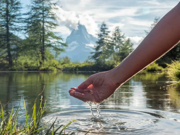 Female hand cupped catching fresh water from mountain lake