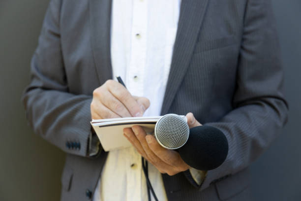 istock Reporter at press conference or media event, writing notes, holding microphone 1278395368