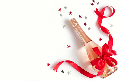 Champagne bottle with red bow and stars isolated on white background. Campagne for Christmas or Birthday celebration, top view, copy space.