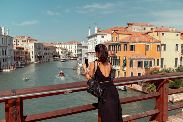Young woman taking a photo of Venice canal with mobile phone