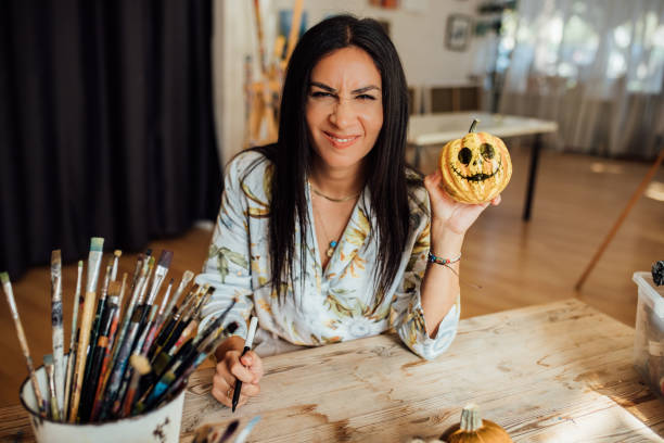 Female hands drawing a face on pumpkin and preparing to Halloween holiday